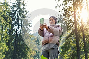 Young adult caucasian beautiful woman in warm jacket and wool suit video chating by cell phone to friends or family during walk in