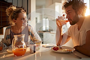 Young adult caucasian couple having breakfast in sunny dining room, looking each other, smiling