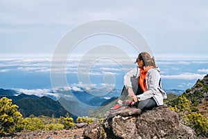 Young adult caucasian female dressed  sporty clothes resting on the rock and enjoying clouds view from Pico Ruivo mount 1861m - photo