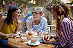 Young adult caucasian female friends talking and laughing in outdoor cafe, drinking coffee. gossip concept