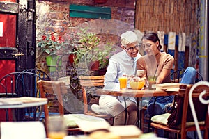 Young adult caucasian female showing something on her cell phone to elderly woman, smiling