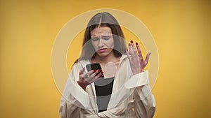 Young adult caucasian woman is upset by the news on her smartphone on a bright yellow background
