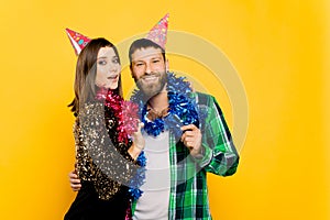 Young adult cheerful guy and girl 20s in party hats and New Year`s tinsel hugging and looking at the camera