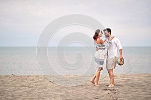 Young adult couple hugging, looking each other, standing barefoot at sandy beach