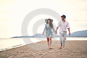 Young adult couple in love walking barefoot on beach, holding hands