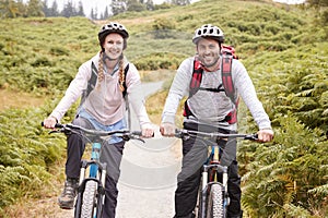 Young adult couple riding mountain bikes in a country lane, looking at camera, close up