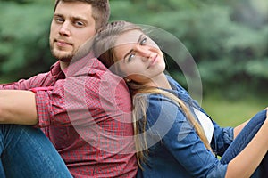 Young adult couple siting back in back in nature