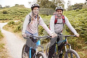 Young adult couple sitting on mountain bikes in a country lane during a camping holiday, close up