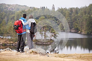 Young adult couple standing on a rock admiring the lakeside view, back view