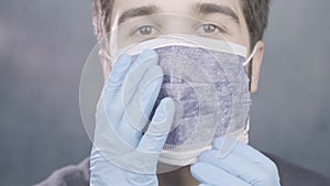 Young adult doctor face close up shows how to wear surgical mask latex gloves on blue