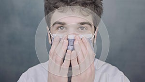 Young adult doctor face close up shows how to wear surgical mask latex gloves on blue