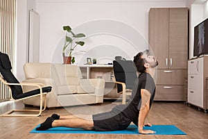 Young adult doing cobra yoga pose on his house floor