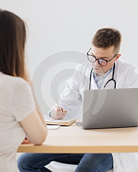 a young adult European and competent doctor in a white coat in a medical clinic in his office is seeing a patient