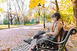 young adult fashion woman sitting at city park bench in autumn fall season