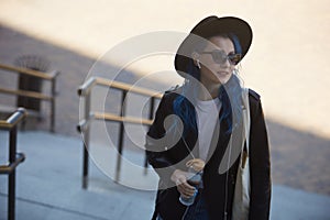 Young adult female with blue hair walking on stairs in the city center with a reusable glass bottle of water and cottong shopper