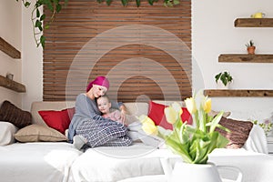 Young adult female cancer patient spending time with her daughter at home, relaxing on the couch.