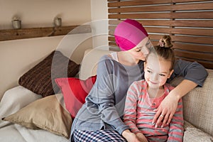 Young adult female cancer patient spending time with her daughter at home, relaxing on the couch. Cancer and family support.