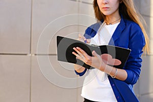 Young adult female girl student holds in hands diary, notebook, Students` work, homework and writes pen against backdrop