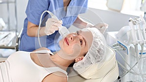 Young adult female patient receiving professional hardware facial procedure at beauty clinic using cooling attachment to