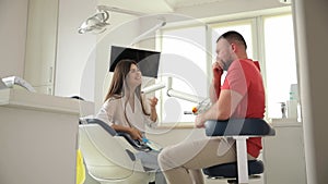 Young adult female patient sitting on dental chair and having conversation with her dentist.