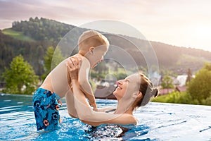 Young adult female person enjoy having fun swimming with happy little child at luxury outdoor swimming pool against fog