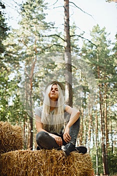 Young adult female sitting with her eyes closed on a haystack outdoors