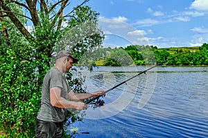 Young adult fisherman casts a fishing rod into the river. Portrait of a man fishing on a background of beautiful juicy green