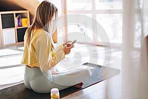 Young adult fitness blonde woman practice morning yoga using mobile phone near the window of home