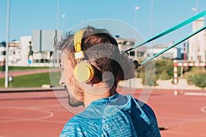 Young adult fitness monitor man, training trx outdoors while listening to music with yellow headphones. Sport and health concept