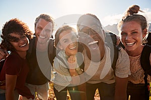 Young adult friends on a hike celebrate reaching the summit, smiling to camera, close up