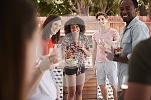 Young adult friends standing with drinks at a backyard party