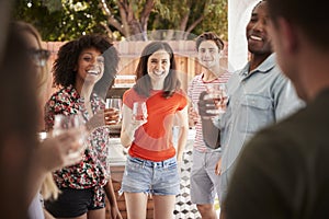 Young adult friends standing with drinks at a backyard party