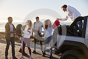 Young adult friends unloading backpacks from the back of car