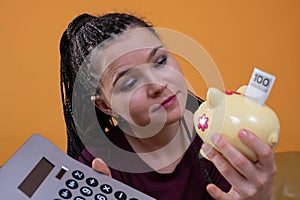 A young adult girl teaches her porcelain piggy bank how to properly save earned money. Teaching finance and cash