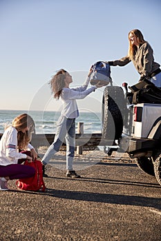Young adult girlfriends unloading luggage from car, vertical