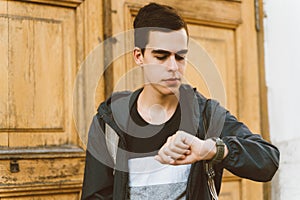 Young adult guy looks at watch. lost time, the concept of lack of time. Stressed caucasian man with black hair afraid of getting