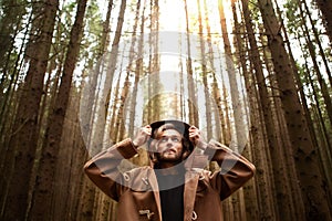 A young adult handsome man, with a mysterious look, in a dark wild forest.