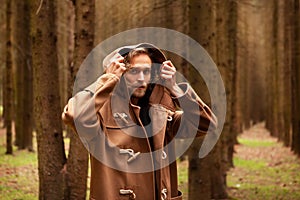 Young adult handsome man, with a mysterious look, in a dark wild forest.