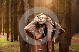 A young adult handsome man, with a mysterious look, in a dark wild forest.