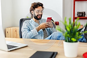 Young adult handsome man using smart phone device sitting at desk