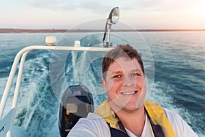 Young adult happy caucasian excited man portrait enjoy having fun driving fast motorboat on pond water surface at sunset