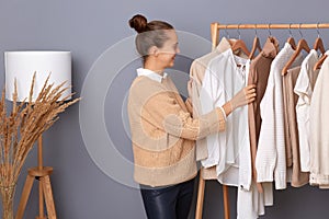 Young adult happy woman with bun hairstyle professional expert fashion stylist standing near clothes hang on shelf in designer