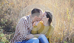 Young adult kissing love couple, have a rest outdoor, sitting on grass