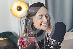 Young adult latin american woman in modern living room recording song using professional headphones and microphone