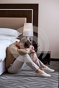 young adult loneliness sad man sitting on floor in bedroom with head bowed