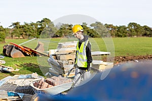 A young adult male builder wearing a high visibility vest and hard hat pushing a wheelbarrow full of bricks while on a building