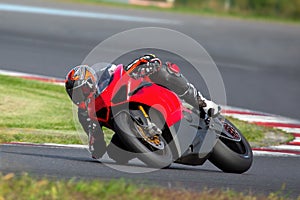 Young adult male is driving a red sports motorcycle on a sharp corner during the race