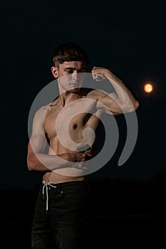 Young adult male flexing his arm muscles at twilight