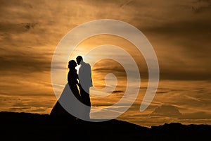 Young adult male groom and female bride holding hands on beach at sunset.