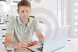 Young adult male shopping online with credit card using laptop at home. Man holding credit card and typing on computer